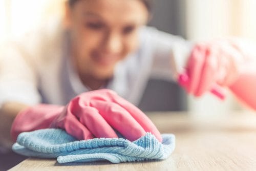 Close up of a woman cleaning a surface with pink gloves and a blue cloth
