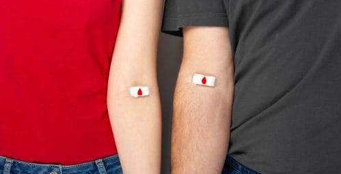 Two people's arms with bandaids that feature a red heart in blood